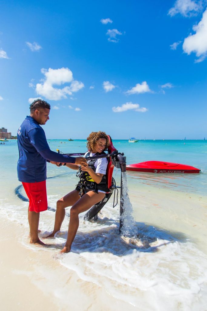 Een medewerker van Red Sail helpt een vrouwelijke toerist opstaan met een waterjetpack.